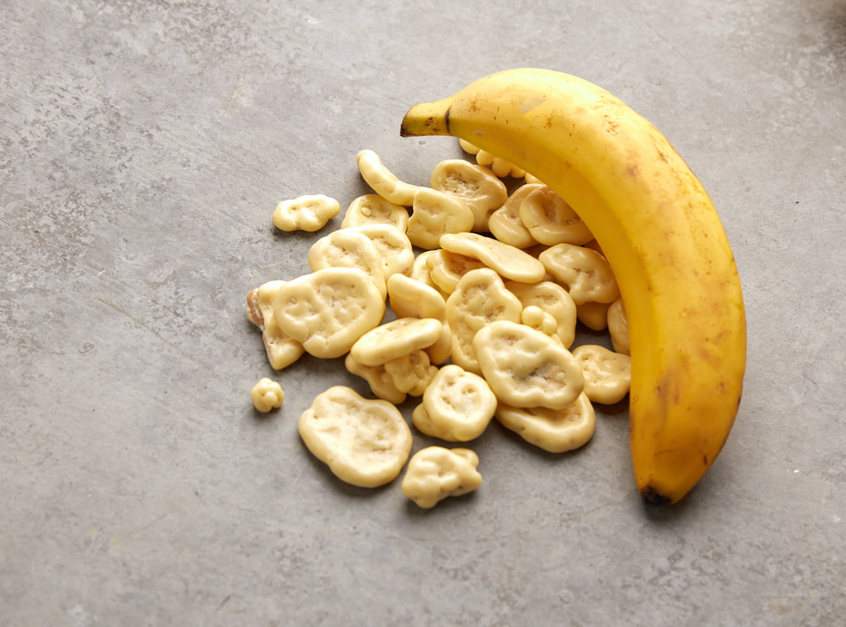 Weiße Schoko-Bananenchips von NESSLIM neben einer frischen Banane, passend als Dessert-Topping oder zum Kaffee.