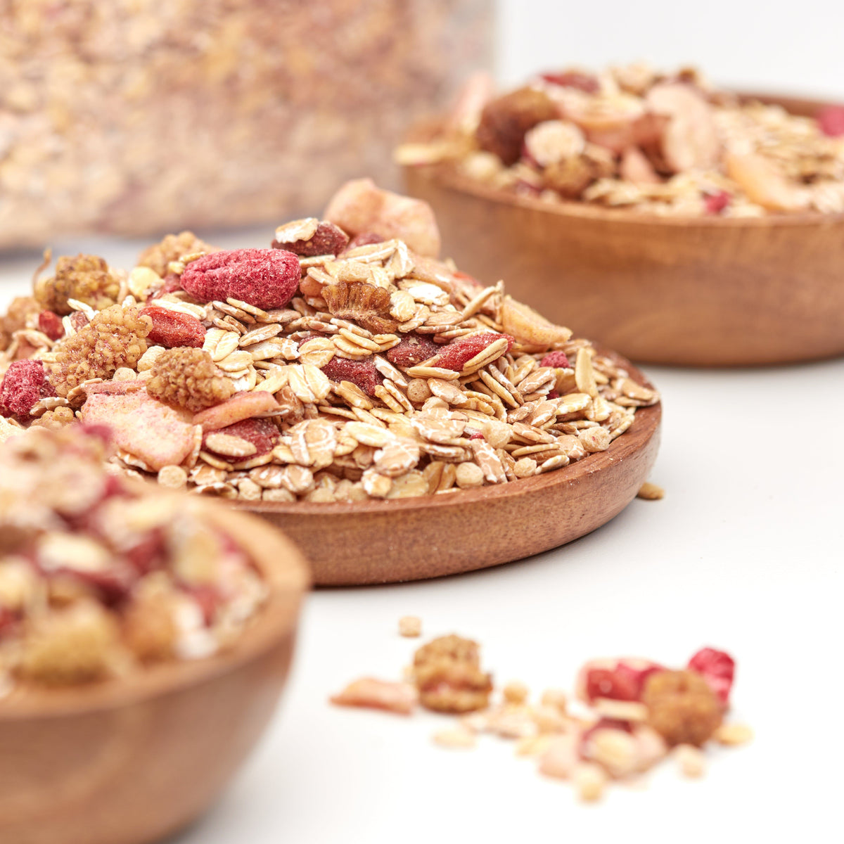 Berry & Fruit Müsli von NESSLIM mit knusprigen Flocken, Beeren und fruchtigen Zutaten auf einem Holzteller.