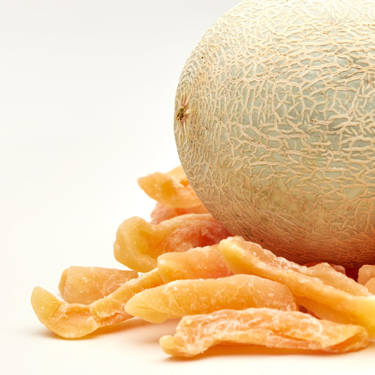Getrocknete Cantaloupe-Melonenstreifen mit Zuckerüberzug vor einer ganzen Melone mit netzartig strukturierter Schale.