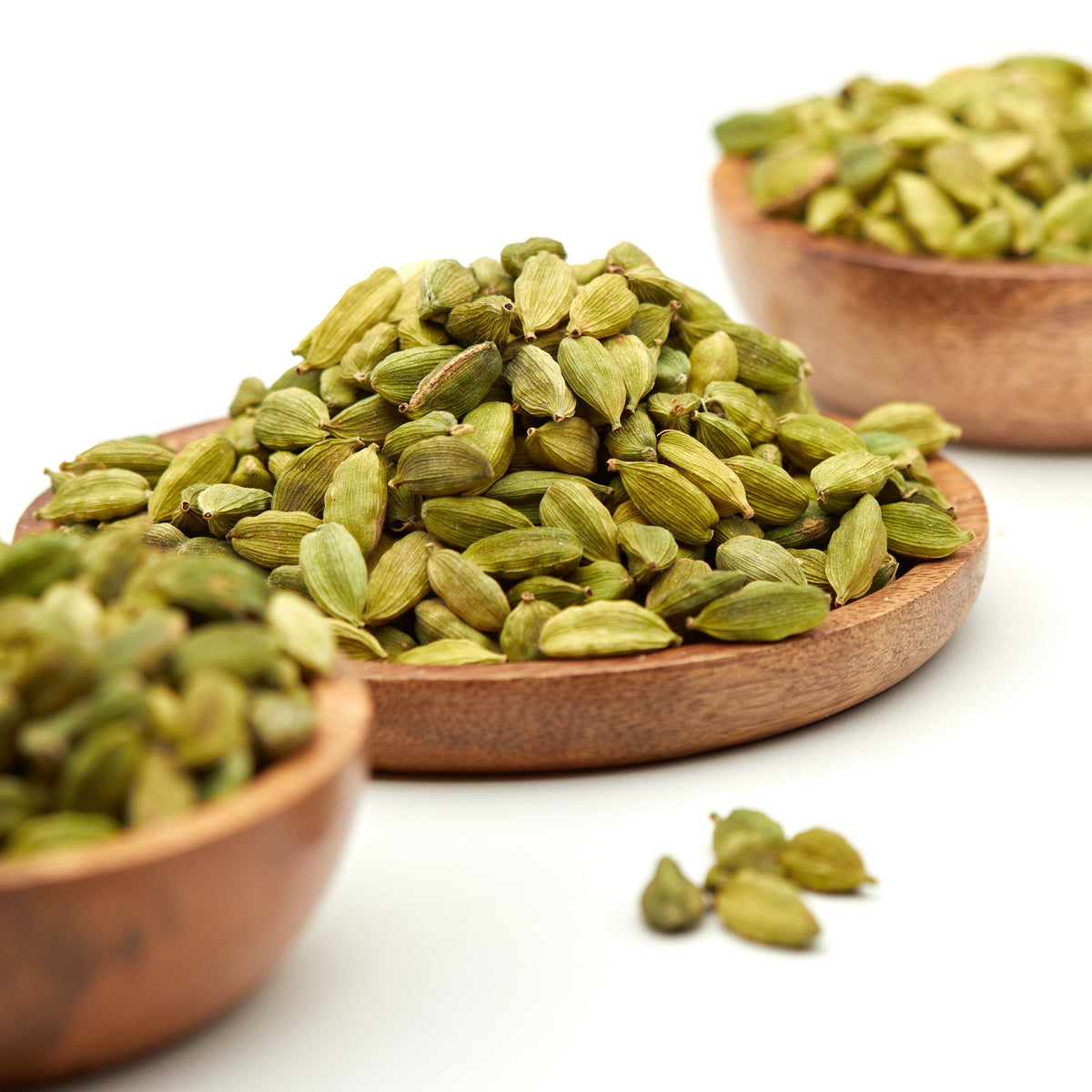 Ganzer grüner Kardamom von Nesslim mit aromatischen Kardamomkapseln in Holzschalen und einzelnen Kapseln im Vordergrund