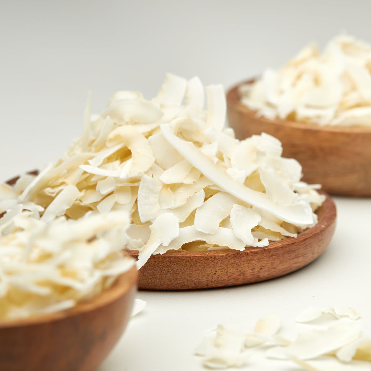 Weiße Kokoschips natur von NESSLIM ohne Zuckerzusatz, auf einem Holzteller und in Holzschalen angerichtet.
