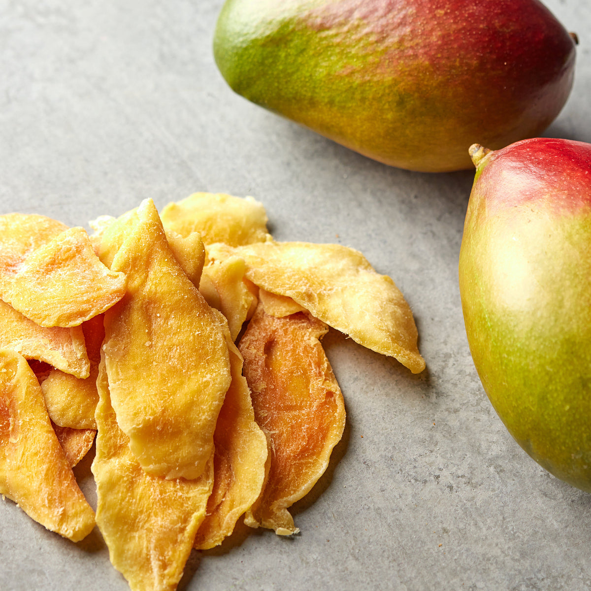 Kandierte Mangoscheiben von NESSLIM neben frischen Mangos für Desserts und Snack-Mixe.