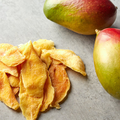 Kandierte Mangoscheiben von NESSLIM neben frischen Mangos für Desserts und Snack-Mixe.