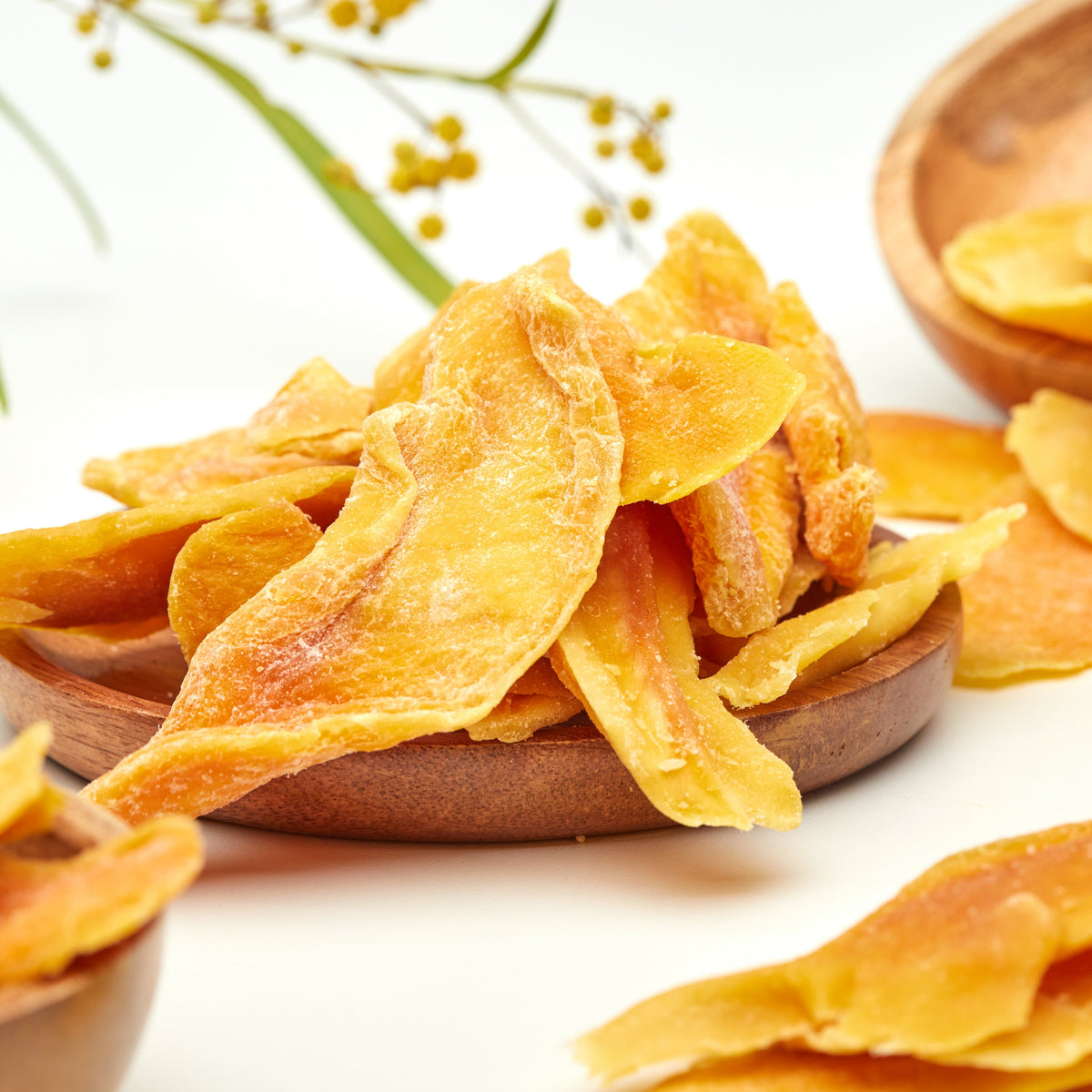 Saftig kandierte Mangoscheiben von NESSLIM in Holzschalen als fruchtig-süßer Juicy-Snack.
