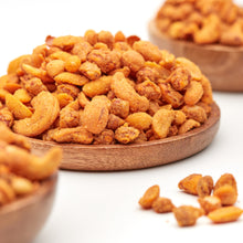 Nussmix Spicy Chili von NESSLIM mit würzigen Erdnüssen und Cashewkernen auf einem Holzteller.