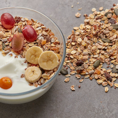 Premium Müsli von NESSLIM auf einer Joghurt-Bowl mit Banane, Trauben und Physalis als Frühstücksidee.