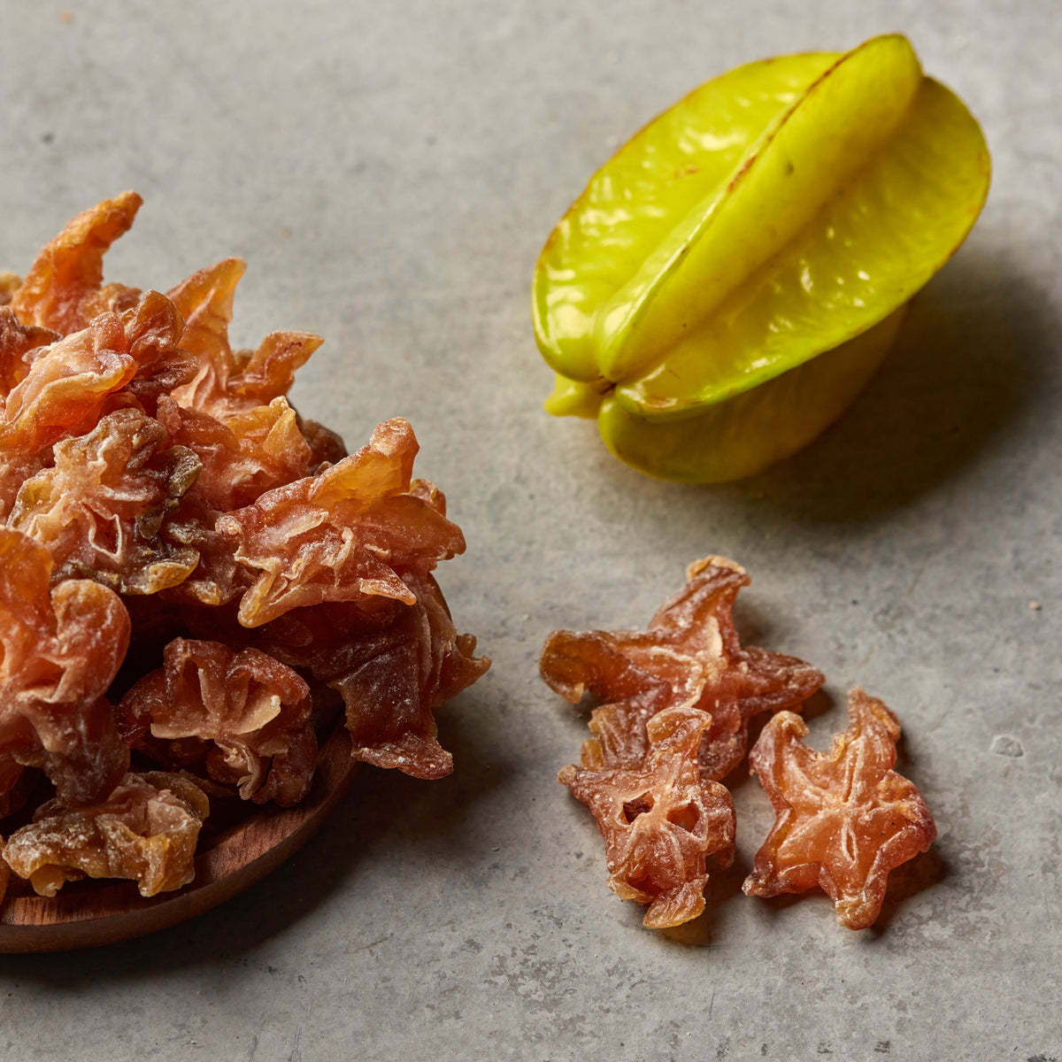 Kandierte Sternfrucht von NESSLIM auf grauer Steinplatte als exotische Garnitur für Drinks und Dessertkreationen.