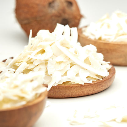 Weiße Kokoschips von NESSLIM als knuspriges Topping für Bowl, Müsli und Joghurt, mit einer ganzen Kokosnuss im Hintergrund.