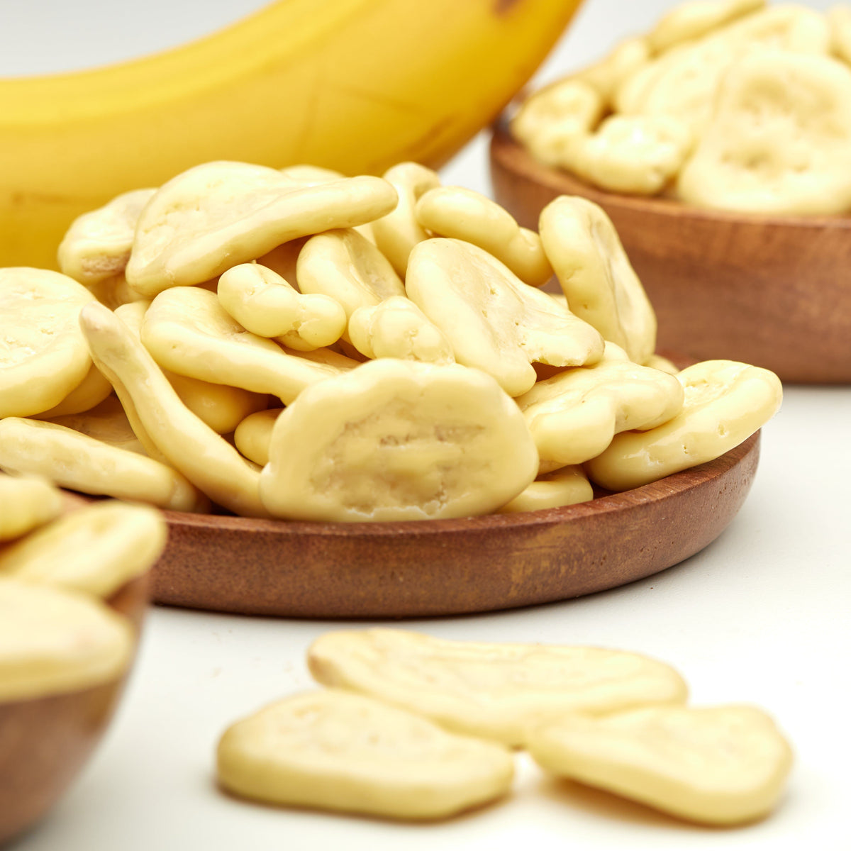 Bananenchips in weißer Schokolade von NESSLIM neben einer frischen Banane, als süßer Snack mit tropischer Note.